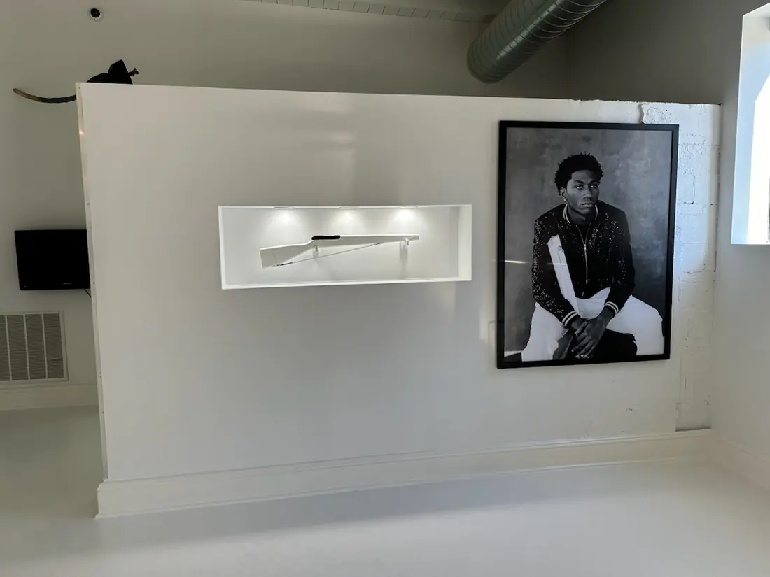 Long white gallery with framed photographs hung in a single line and a low bench.